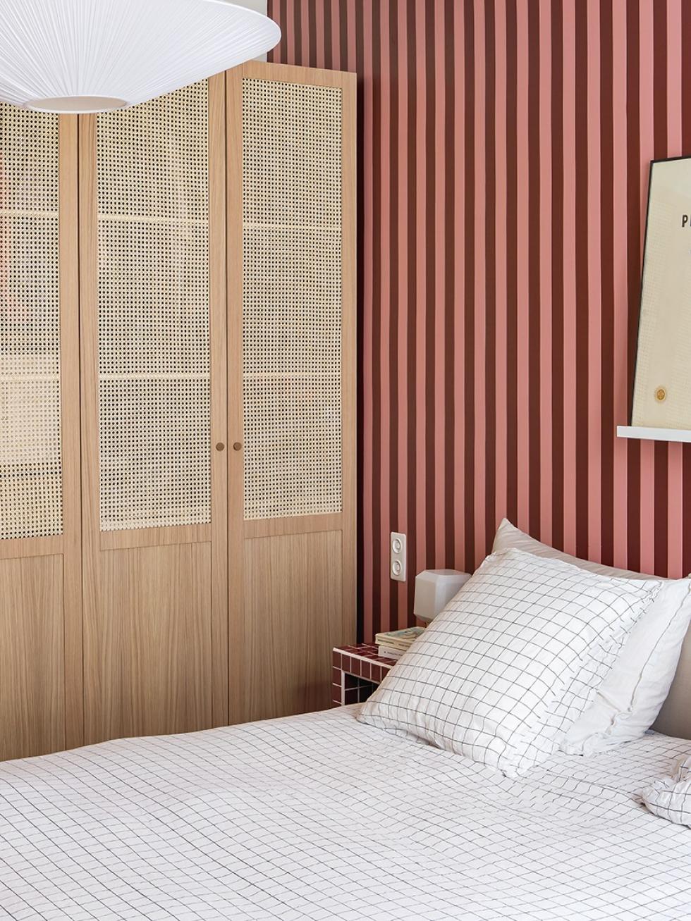 Das Schlafzimmer von Lisa Gachet, mit bordeauxroter und rosafarbener Tapete, und einem Kleiderschrank aus Flechtdesign und Eiche Natur.