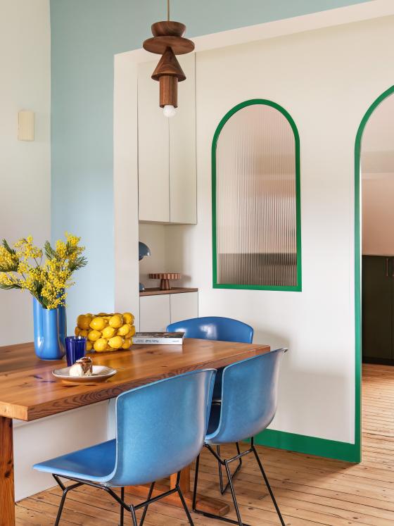 Salon avec cheminée recouverte de faïence, table et chaises colorées.